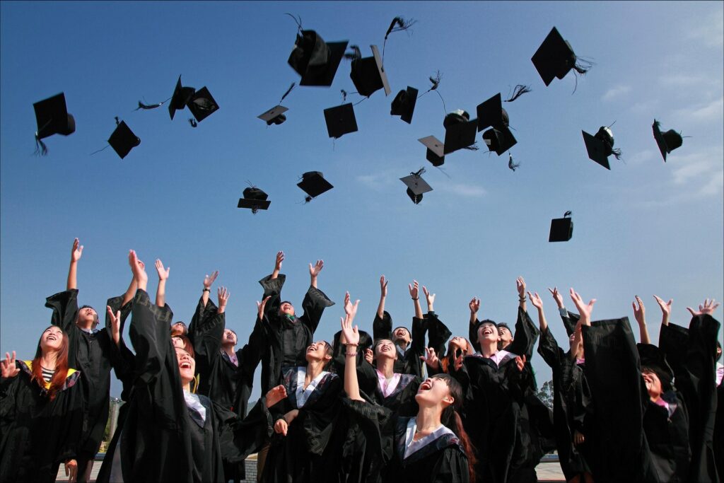 ブラックアカデミーのガウンを身に着けている新しく卒業した人々が空中に帽子をかぶっています
