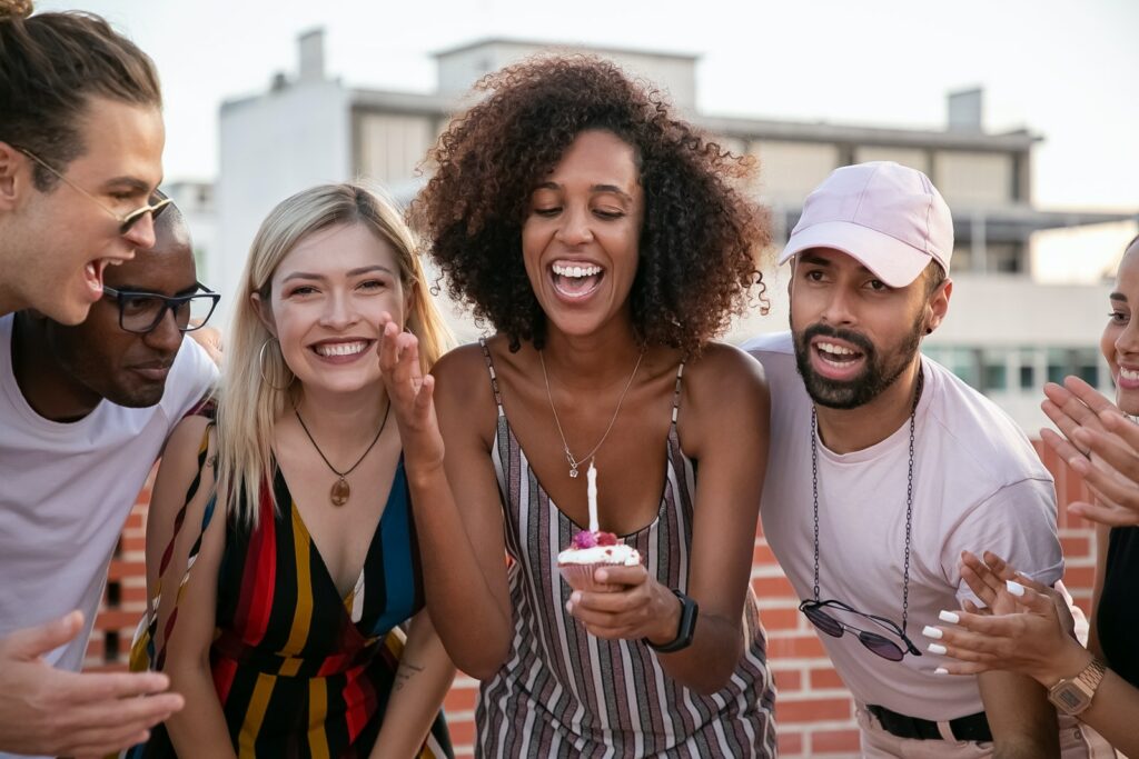 Farklı arkadaşlarıyla doğum günü partisinde mum üfleyen mutlu Afro-Amerikan kadın