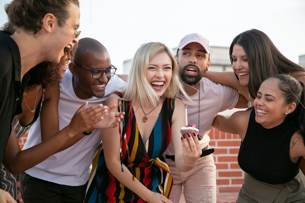 Emocionados jóvenes amigos diversos celebrando el cumpleaños de una alegre mujer en una terraza