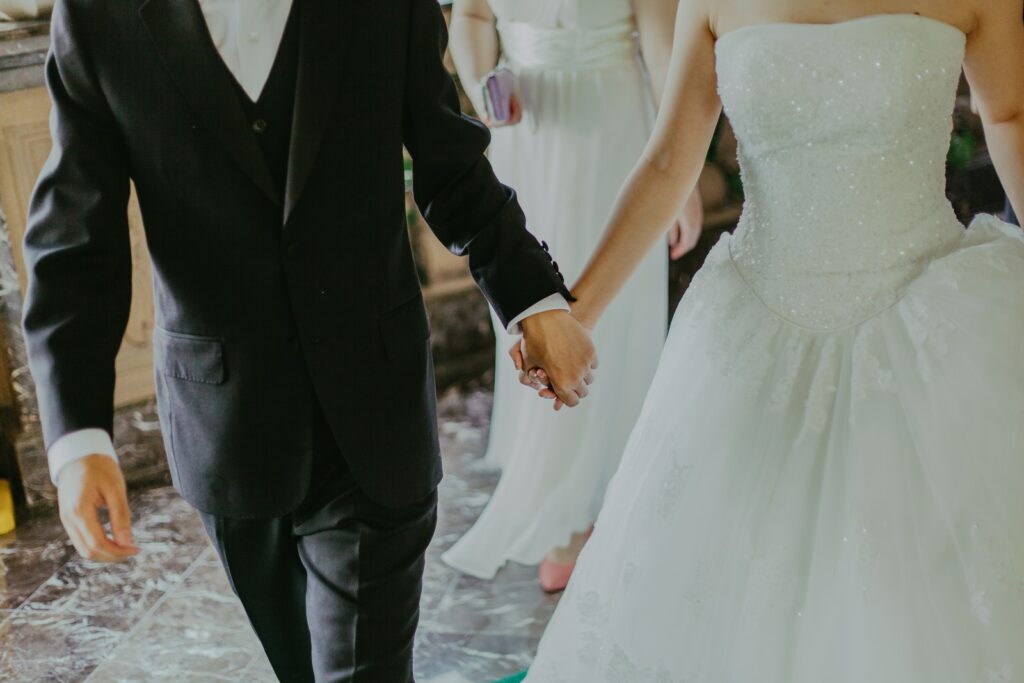Frau in weißem Hochzeitskleid hält Händchen mit Mann beim Gehen