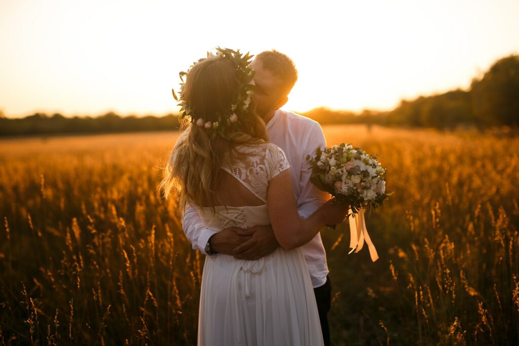 Hombre y mujer de pie frente a un campo de hierba marrón besándose