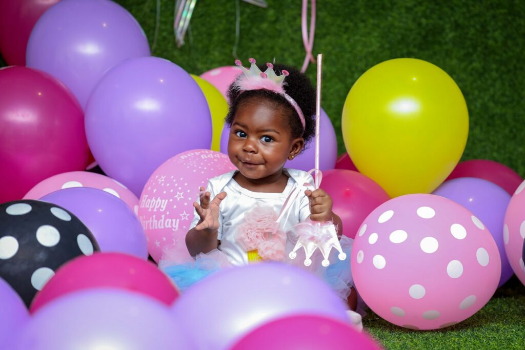 Kleinkind Mädchen sitzt auf dem Boden umgeben von Luftballons