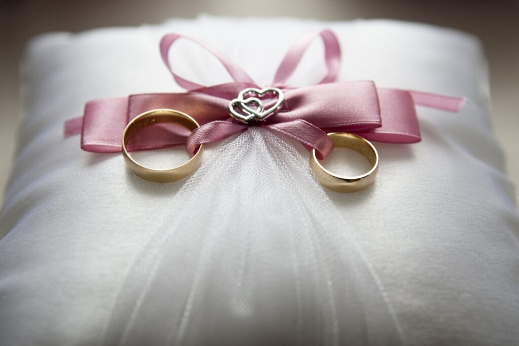 Fotografía de enfoque selectivo del conjunto de anillos de compromiso de color plateado con acento de lazo rosado sobre un cojín.