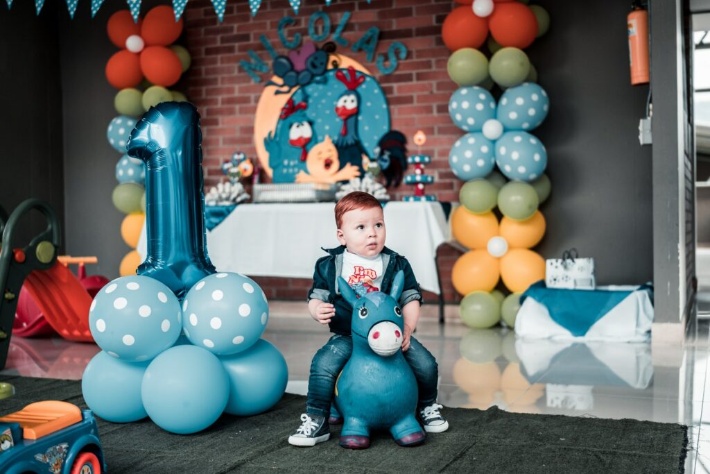 Foto eines Kindes, das auf einem Spielzeug in der Nähe von Luftballons sitzt