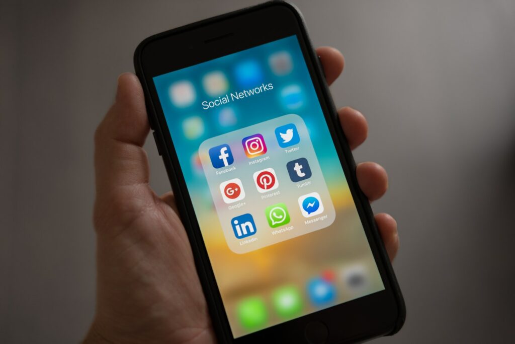 Persona che tiene in mano un Iphone che mostra la cartella dei social network