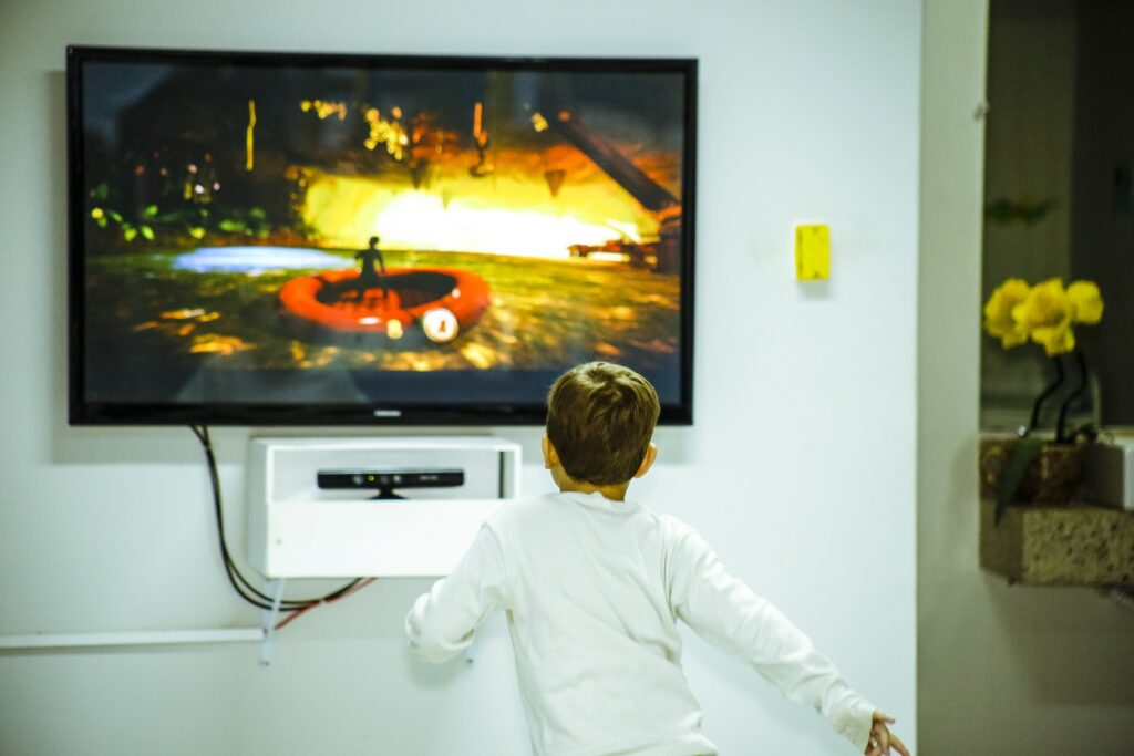 Niño de pie frente a la televisión de pantalla plana