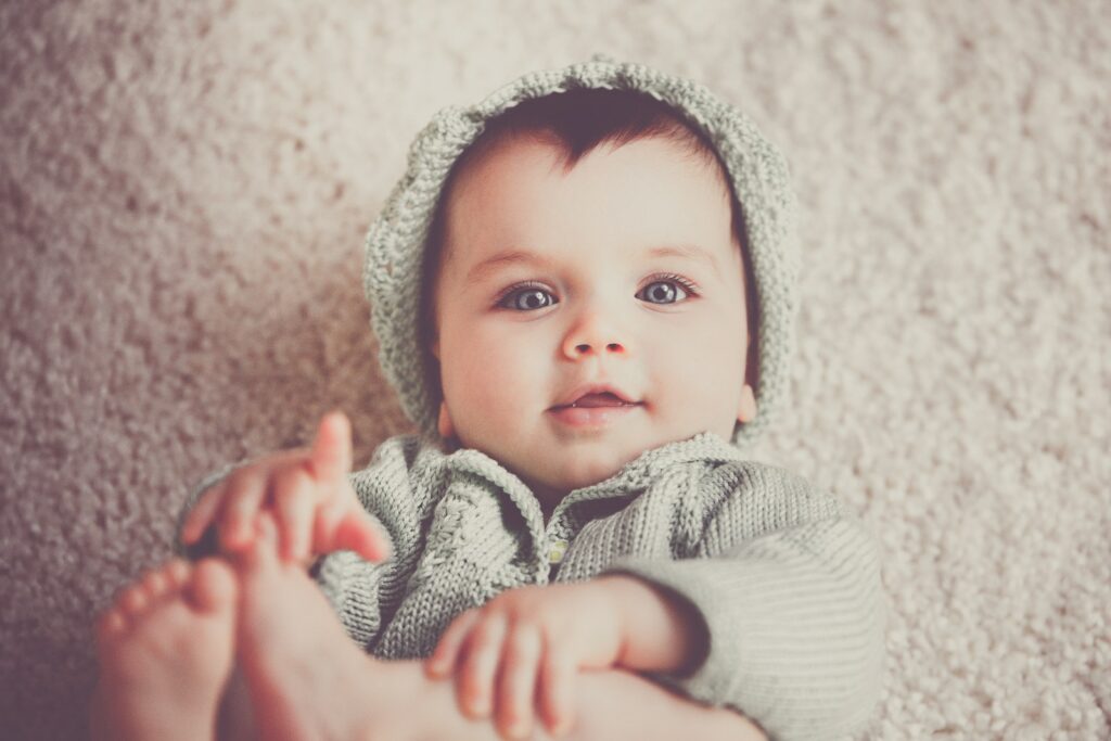 Baby auf grau gestrickter Kapuzenkleidung auf Teppich liegend