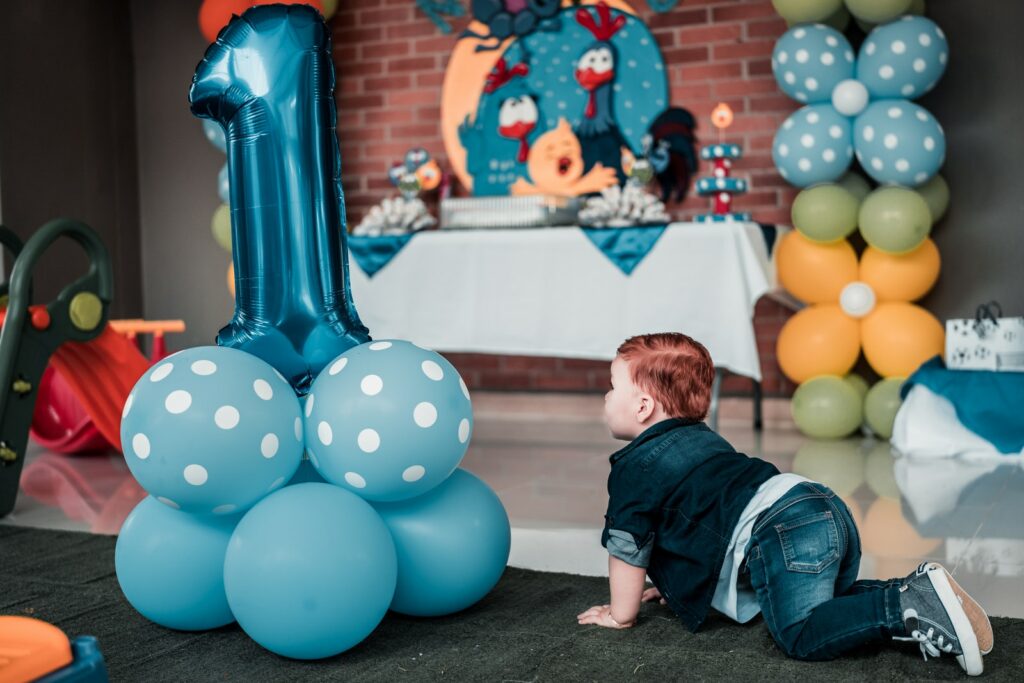 Ребенок в синей джинсовой куртке ползает по полу рядом с воздушными шарами