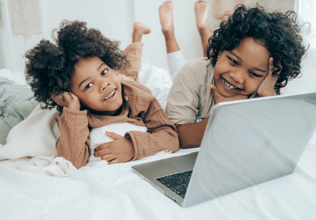 Garçons noirs souriants regardant une vidéo amusante sur un ordinateur portable sur un lit