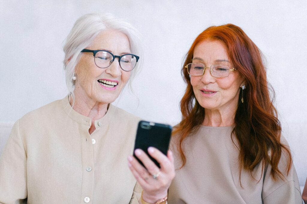 Donne di età allegra che sorridono e guardano video online su smartphone