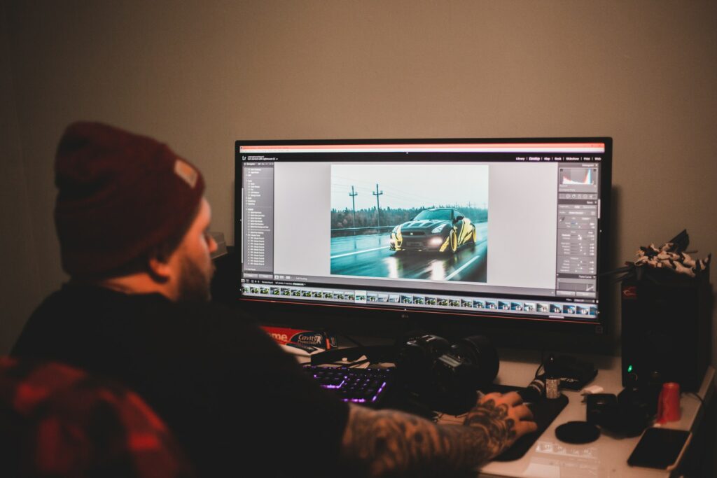 Неузнаваемый татуированный мужчина сидит за столом и работает на компьютере с монтажным видео спортивного автомобиля