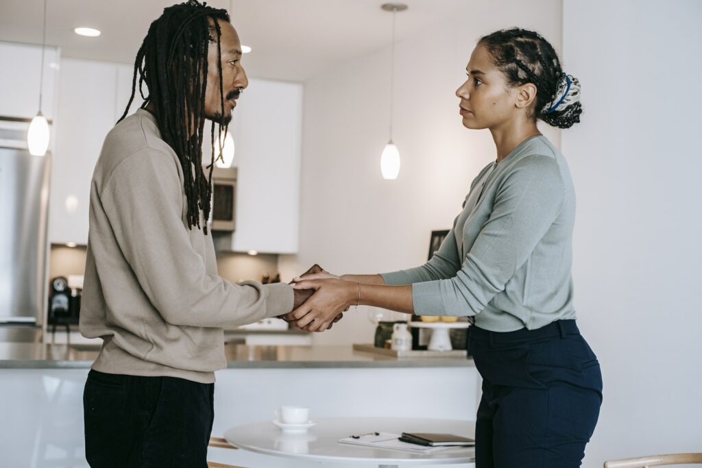 Vue latérale positive d'un client multiethnique et d'une psychothérapeute en vêtements formels se serrant la main et se regardant l'un l'autre après une séance de psychothérapie dans un studio moderne et lumineux.