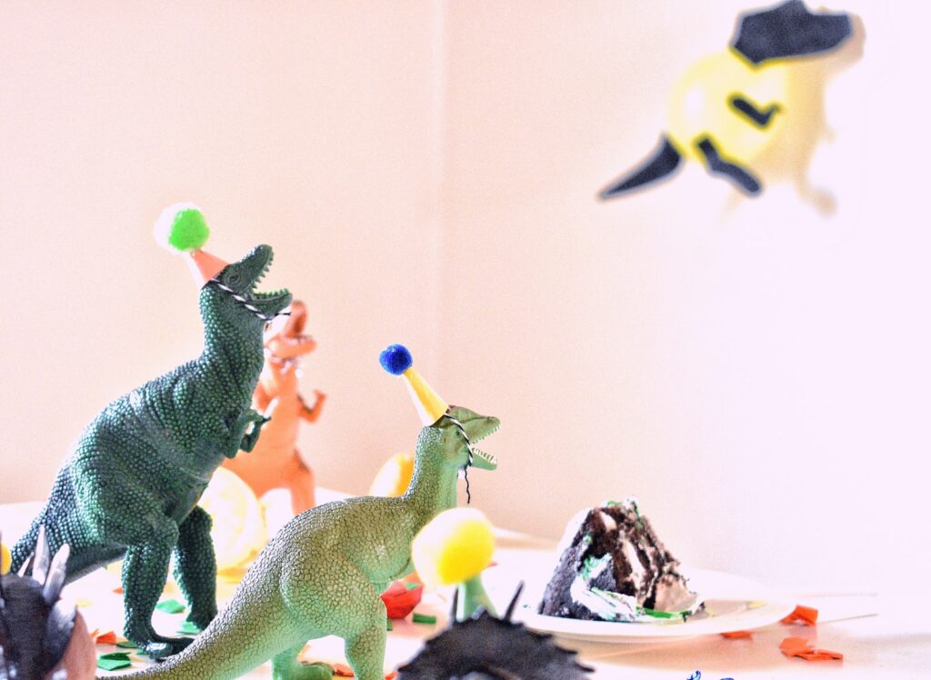 jouets de dinosaures de couleurs assorties près d'une tranche de gâteau sur une table blanche