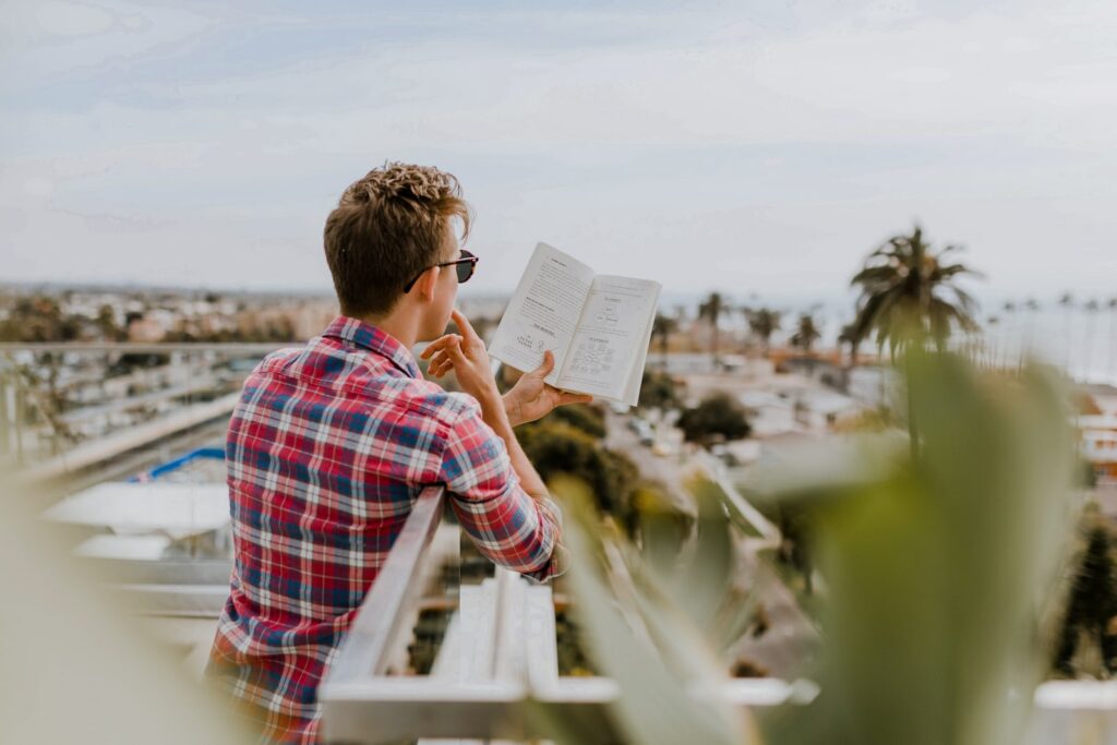 Mann liest tagsüber auf dem Balkon ein Buch