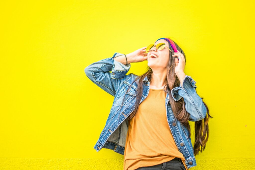 Lächelnde Frau, die aufrecht stehend gegen eine gelbe Wand schaut