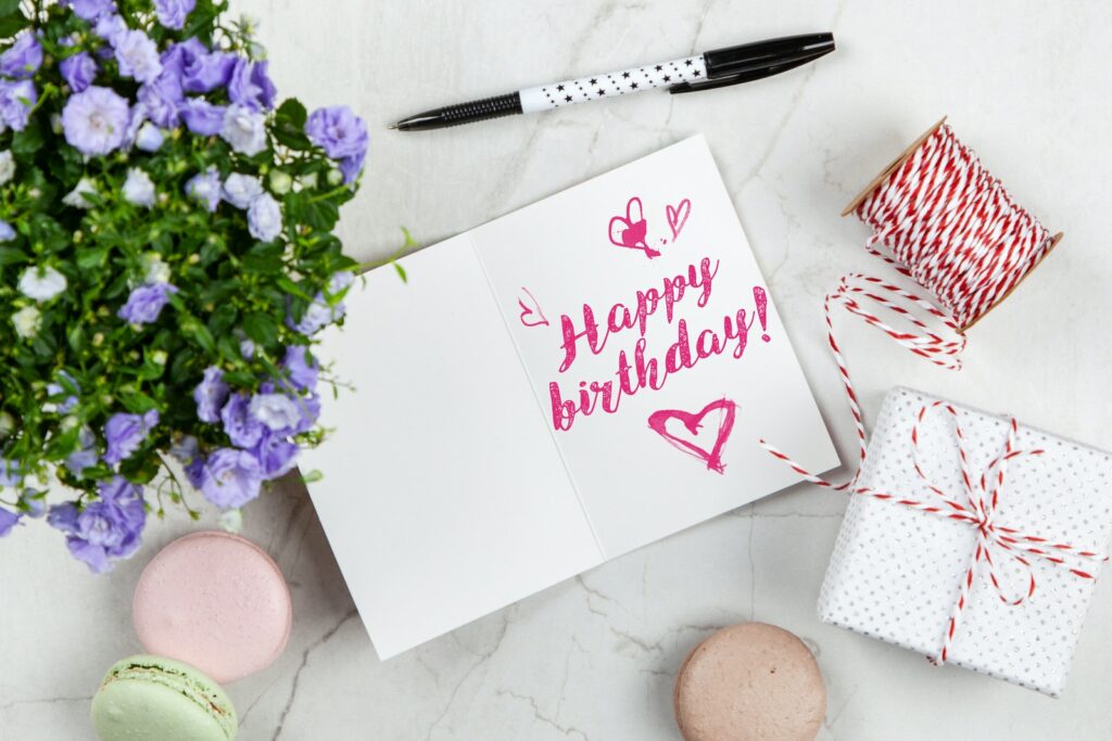 Carte de vœux d'anniversaire à côté d'une fleur, d'un fil, d'une boîte et de macarons