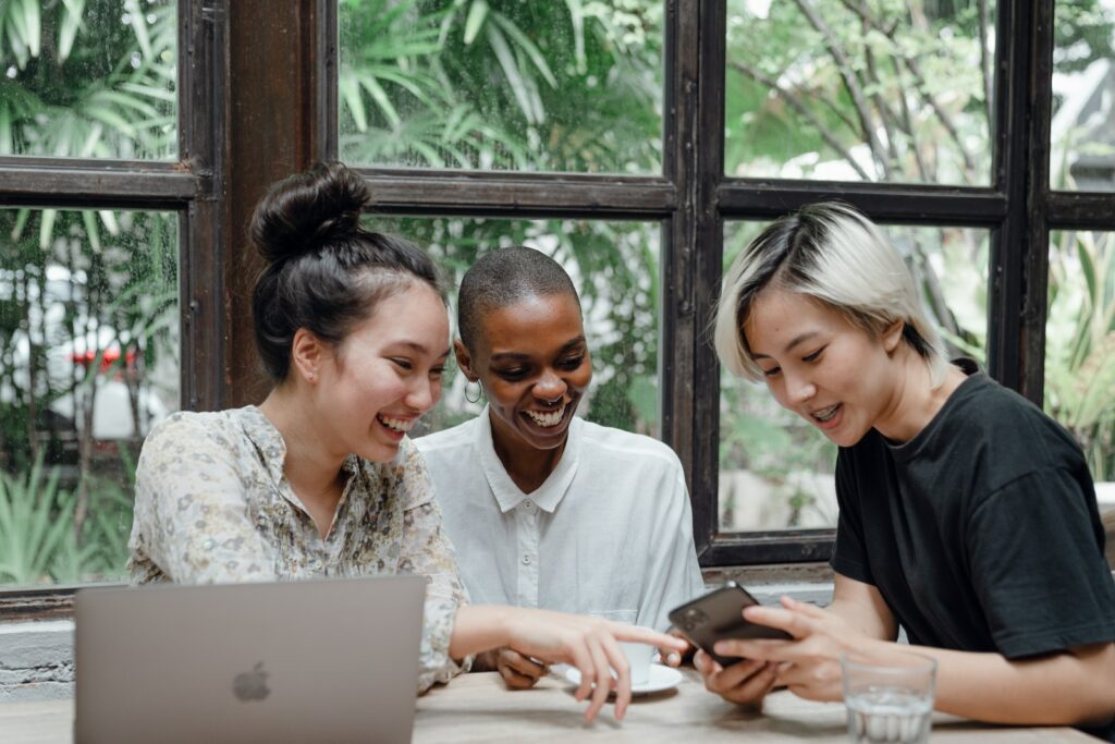 Giovani e allegre amiche diverse che ridono guardando un video divertente sullo smartphone durante una pausa caffè in un accogliente bar