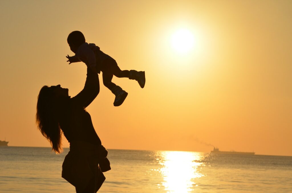 ゴールデンアワーにビーチで赤ちゃんを抱っこする母親のシルエット写真