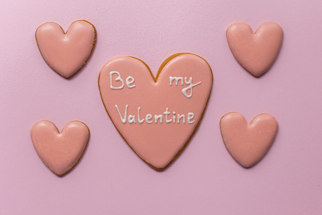 Vista superior de biscoitos em forma de coração doce dizendo Be My Valentine em fundo rosa
