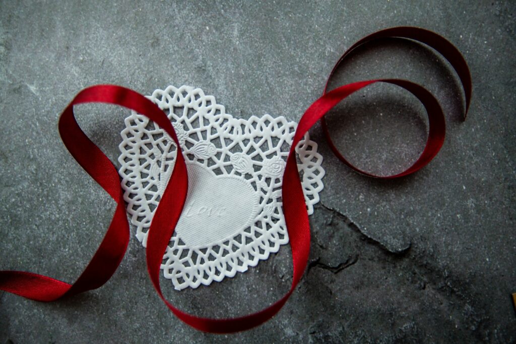 Gri taş masa üzerine yerleştirilmiş, üzerinde Love (Aşk) yazısı ve kırmızı saten kurdele bulunan beyaz kalp şeklindeki kağıt dantelin üstten görünümü