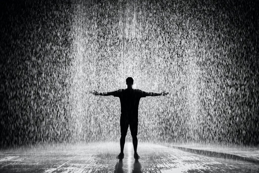 Silhouette e fotografia in scala di grigi di un uomo in piedi sotto la pioggia