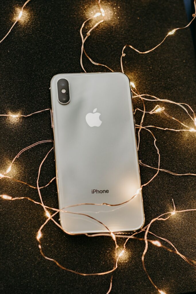 点灯済みのストリングライトに寝そべるシルバーのIphone X