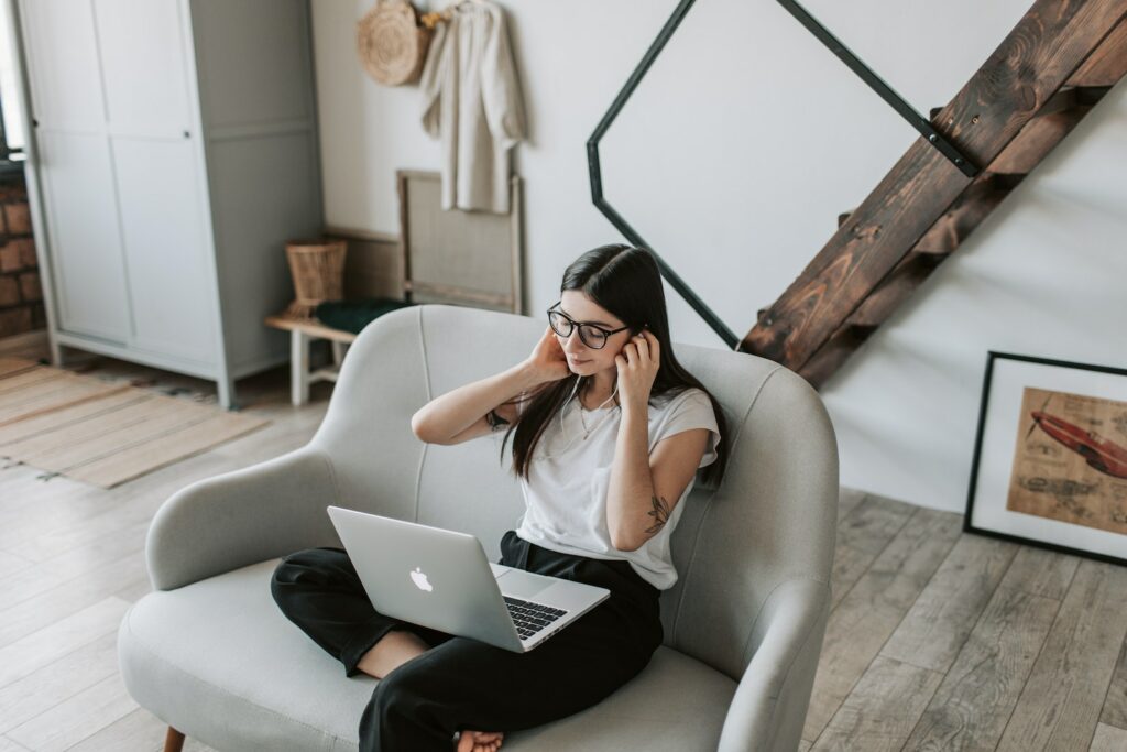 Positive woman using earphones and laptop at home during free time